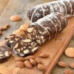 two chocolate salami on wooden board with three slices cut