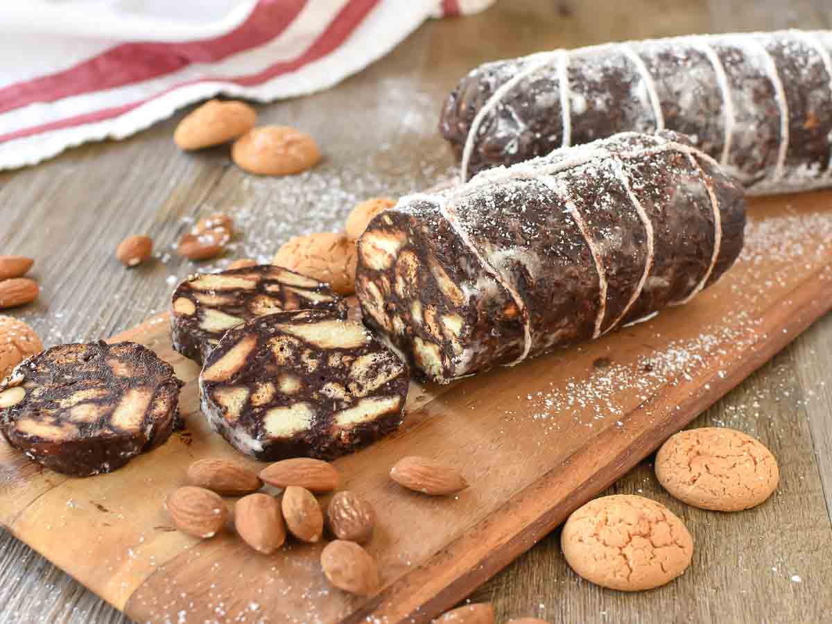 This Chocolate Salami recipe is a fun, no-bake Italian sweet. It's a crunchy treat that is perfect to serve with an after-dinner coffee. #chocolatesalami #italianrecipe #chocolatedessert #chocolatetreat #afterdinnertreat #sweetrecipe Two chocolate logs that look like salami with few slices cut.