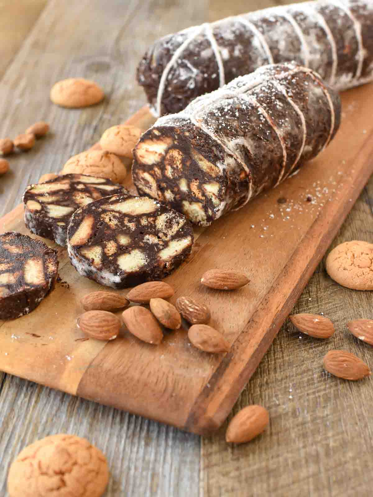 This Chocolate Salami recipe is a fun, no-bake Italian sweet. It's a crunchy treat that is perfect to serve with an after-dinner coffee. #chocolatesalami #italianrecipe #chocolatedessert #chocolatetreat #afterdinnertreat #sweetrecipe Chocolate salami on wooden board with three slices cut.