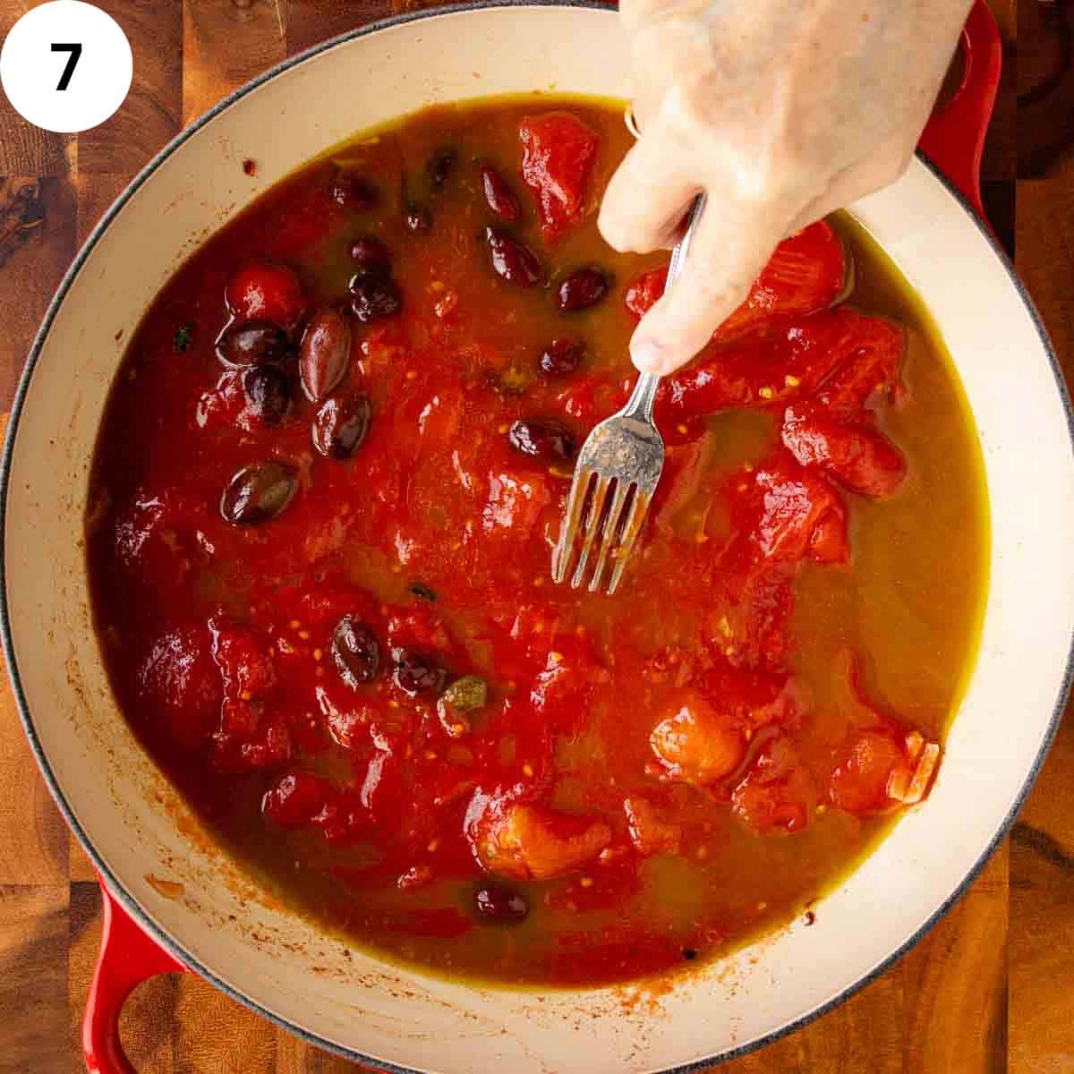 Crushing tomatoes in a pan with a fork.