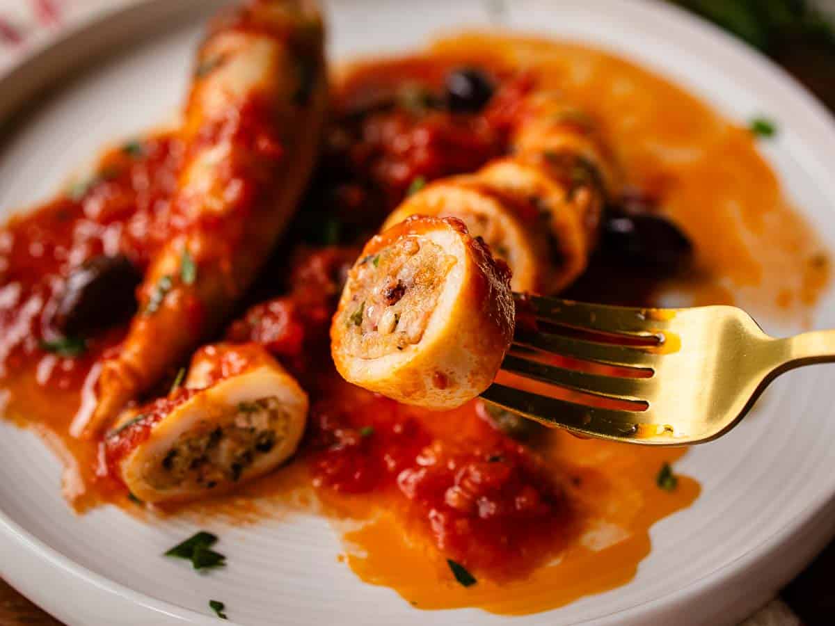 A sliced piece of squid tube that has been stuffed with a bread crumb filling and cooked in tomato sauce.