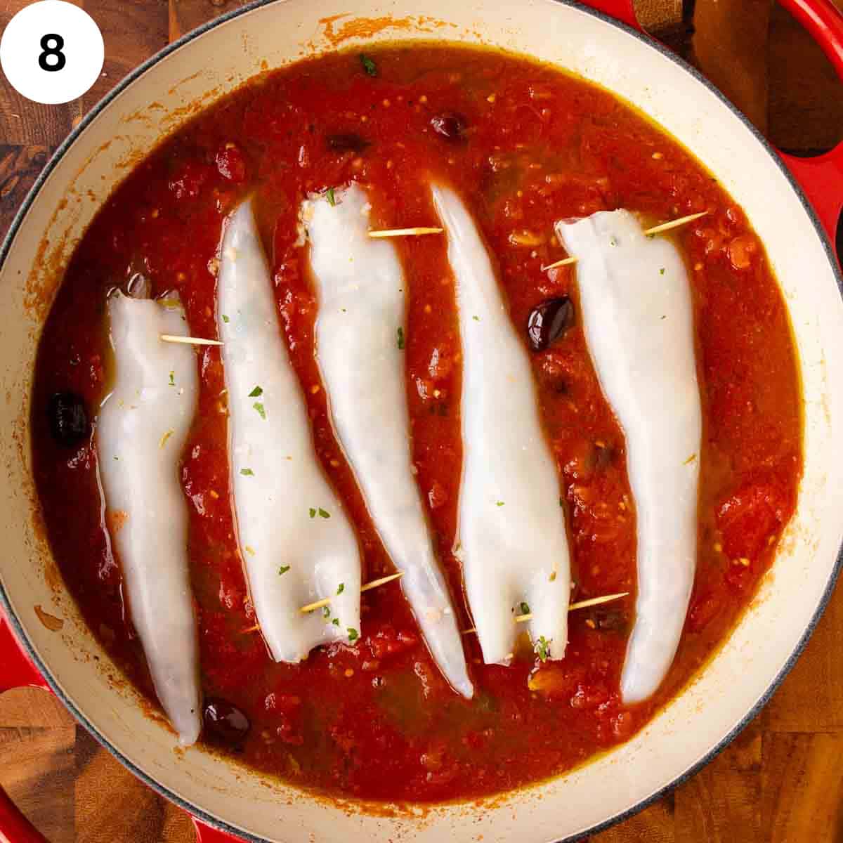 Five filled squid tubes in a pan of tomato sauce.