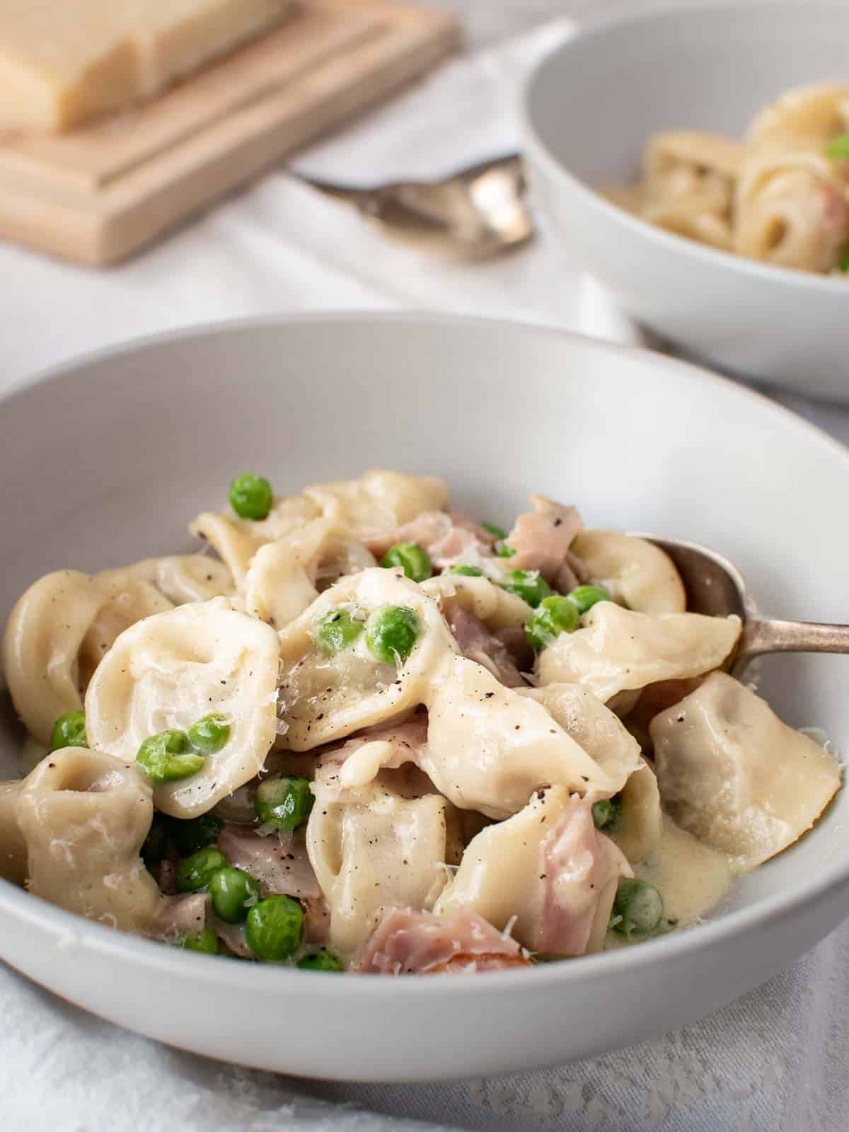Tortellini alla panna in a bowl with peas and ham.
