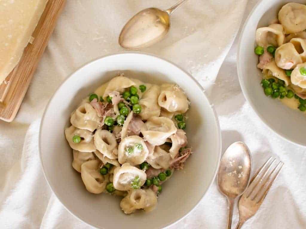 Tortellini with cream, peas and ham in a bowl viewed from above.