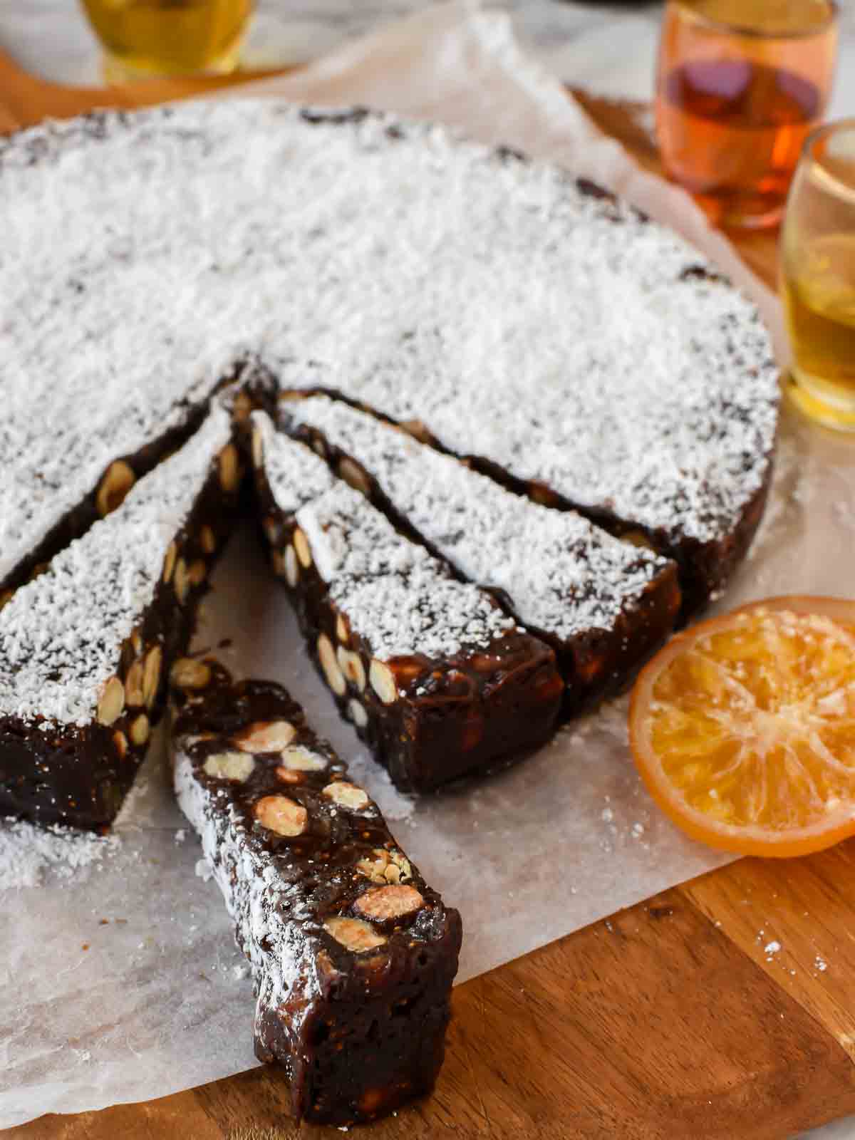 Panforte with Nut and Figs is a Christmas favourite in Italy. Originally from Siena, this rich sweet can now be found throughout Italy and beyond. #panforte #italianchristmas #italianrecipe #panfortedisiena round cake of panforte with a few slices cut.