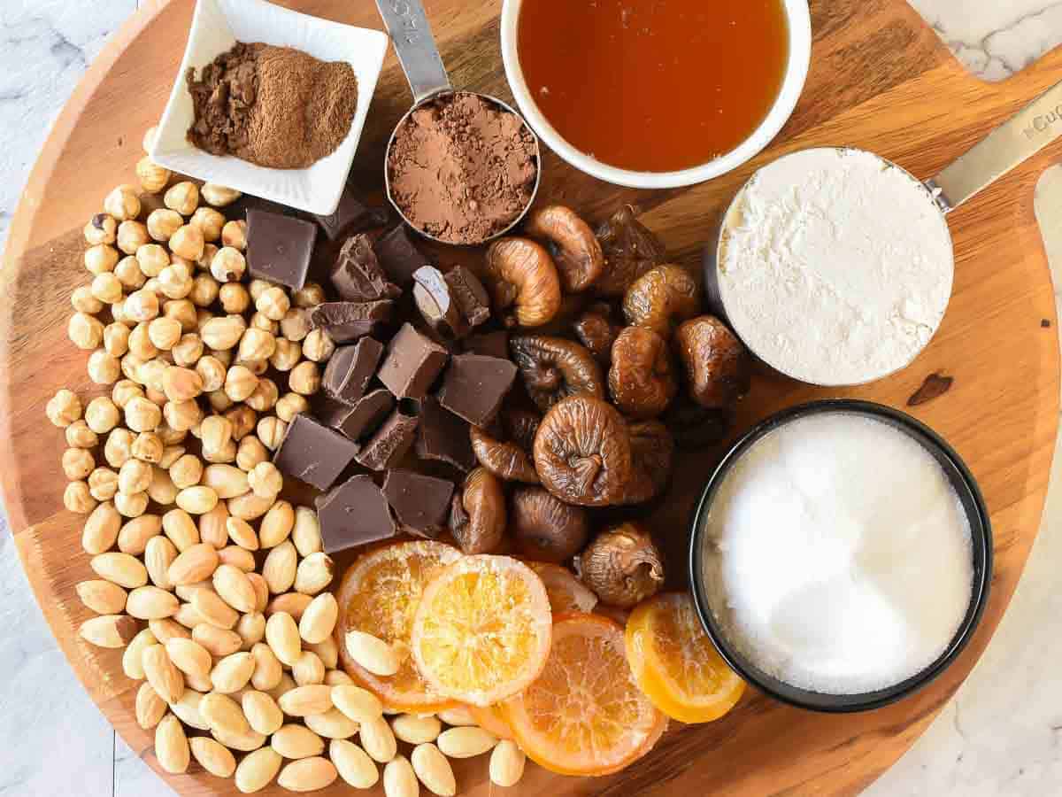 Panforte with Nut and Figs is a Christmas favourite in Italy. Originally from Siena, this rich sweet can now be found throughout Italy and beyond. #panforte #italianchristmas #italianrecipe #panfortedisiena dried figs, nut, honey, sugar, flour, spices and candied oranges viewed from above.