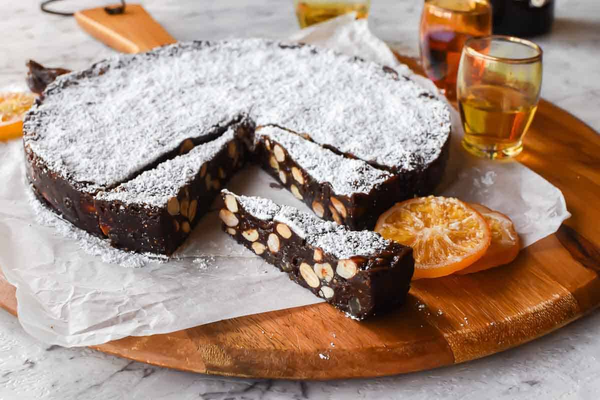 Panforte with Nut and Figs is a Christmas favourite in Italy. Originally from Siena, this rich sweet can now be found throughout Italy and beyond. #panforte #italianchristmas #italianrecipe #panfortedisiena round cake of chocolate and nut confection with a few slices cut.