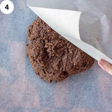 Brown cookie dough being covered by a sheet of parchment paper.
