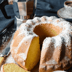 Lemon Yogurt cake with slice in the front and two espresso cups of coffee and moka pot