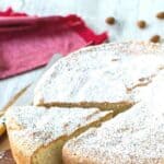 Italian Almond Cake on round wooden board with one wedge cut.
