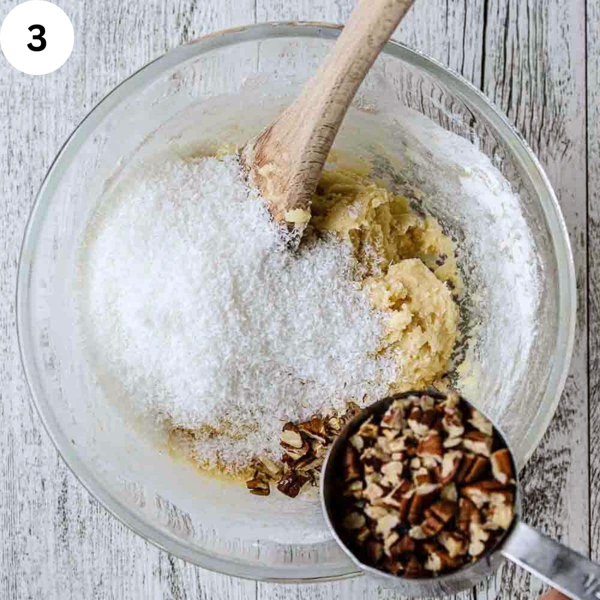 Shredded coconut and chopped pecans being stirred into cookie dough.