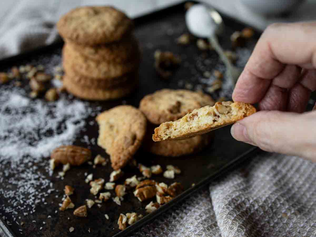 Fingers holding half a cookie with more cookies in the background.