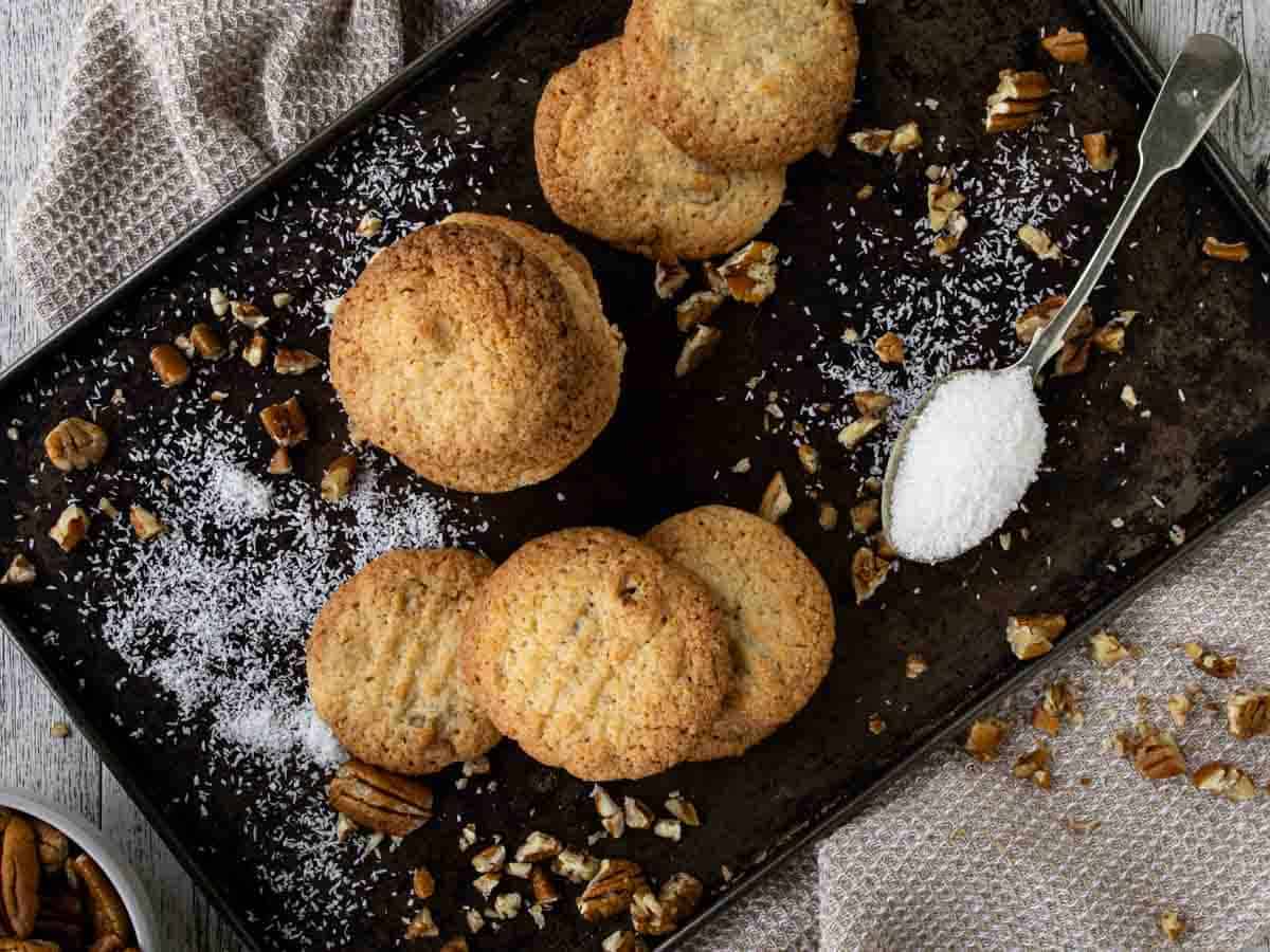 Overhead view of coconut and pecan cookies piled onto a baking sheet.