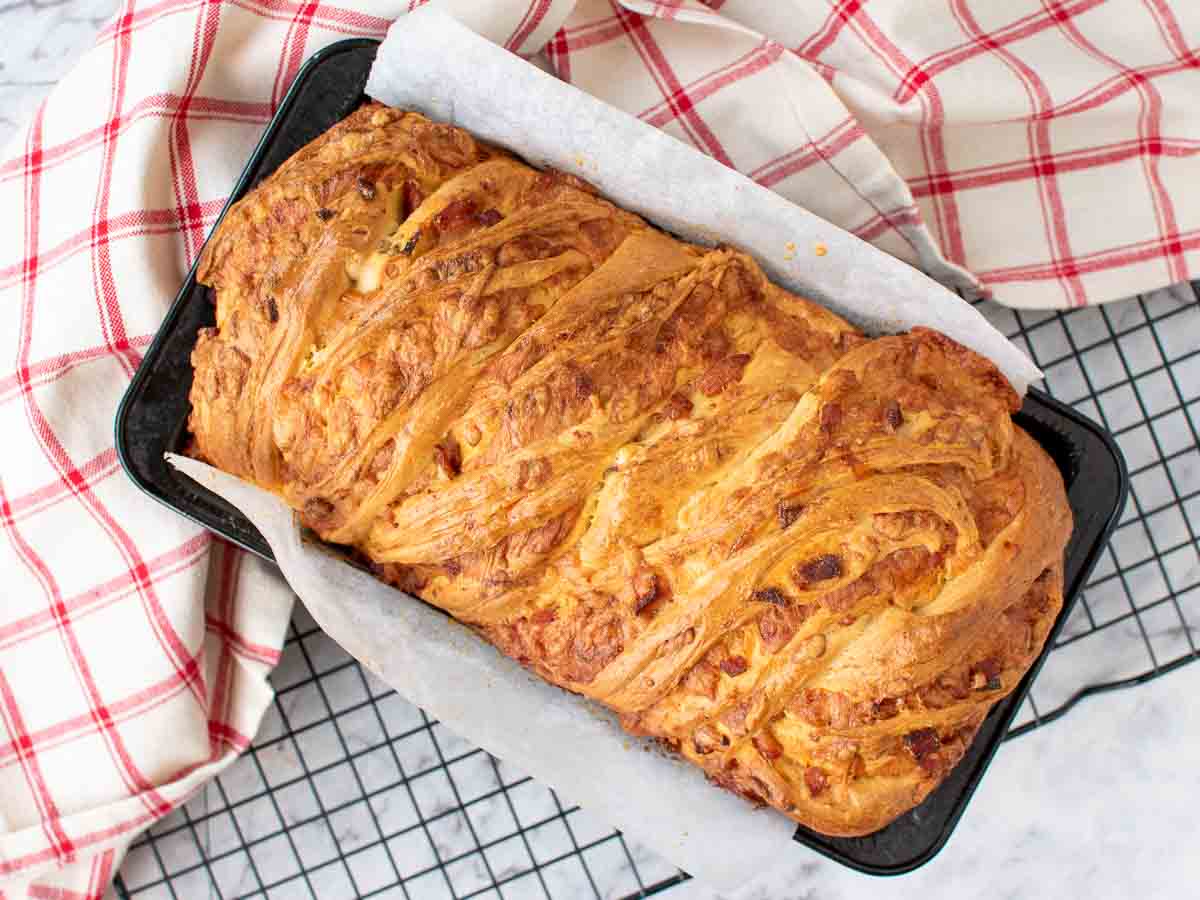 Bread loaf in pan on black wire with red and white cloth rack viewed from above.