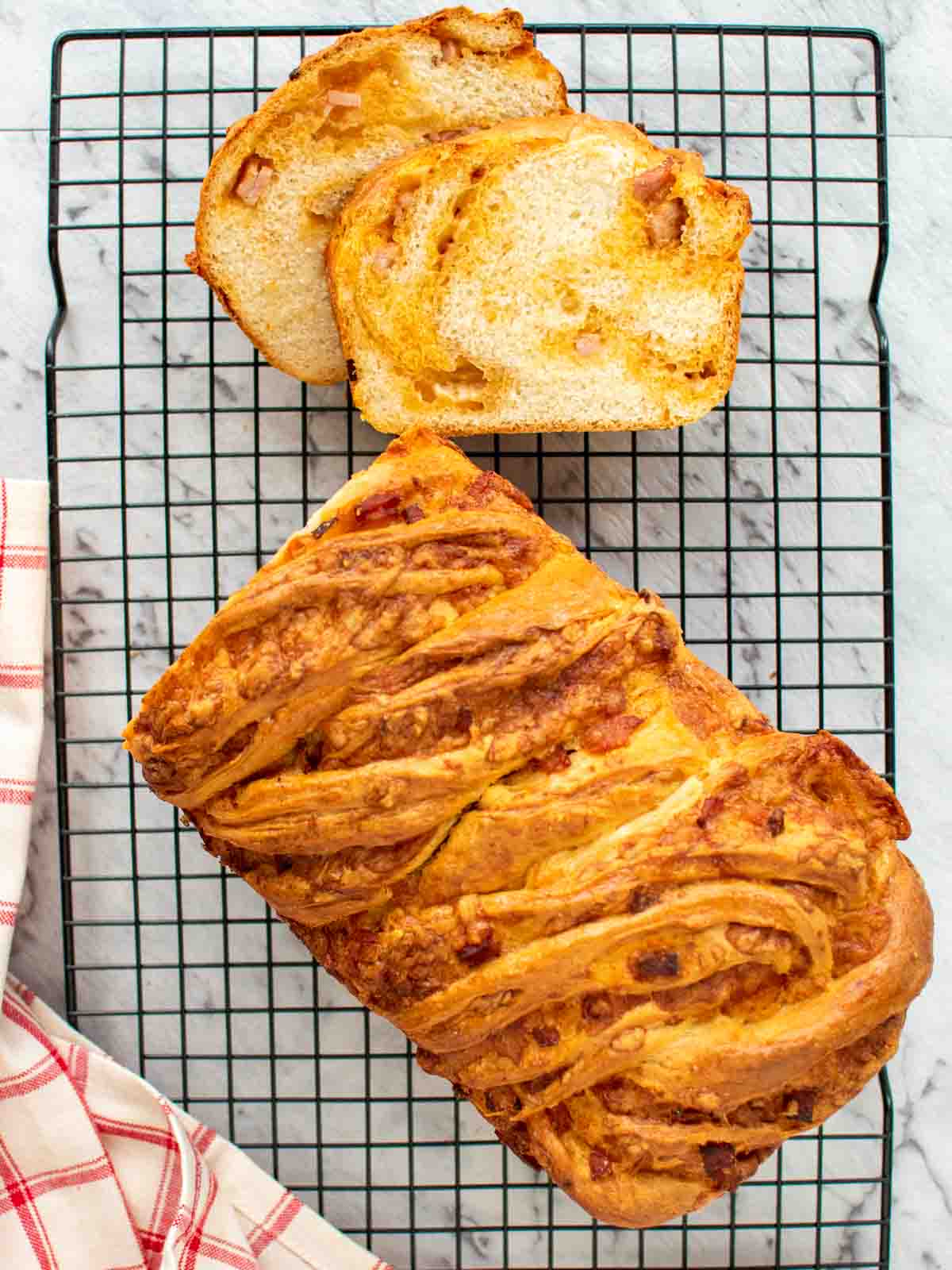 Bacon cheese bread on black wire rack with two slices cut viewed from above.