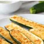 image with text. text reads "easy! roasted zucchini". image is pile of cheese topped zucchini on a white plate with fresh zucchini in background.