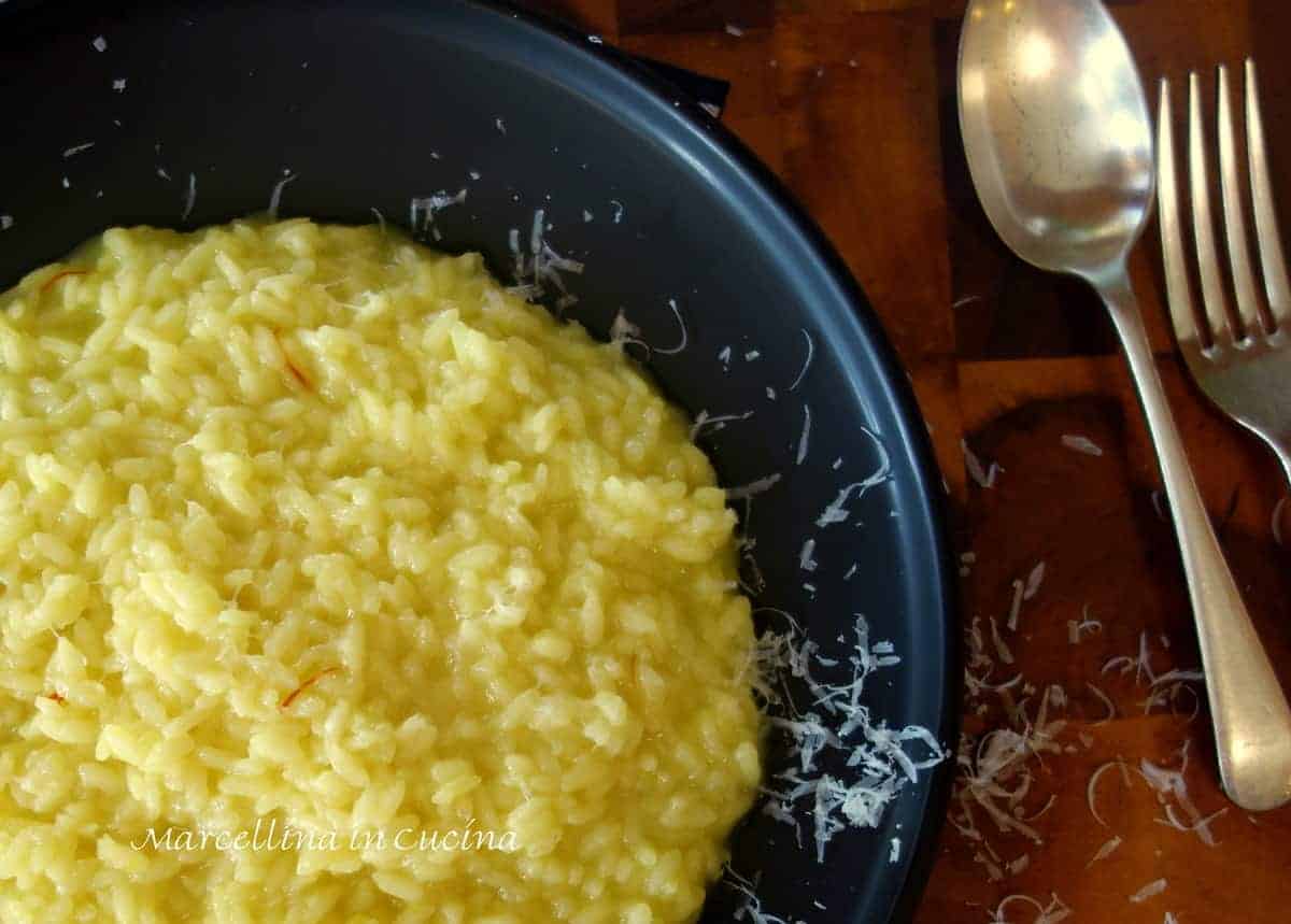 Saffron risotto with grated Parmesan cheese on a black plate with spoon and fork.