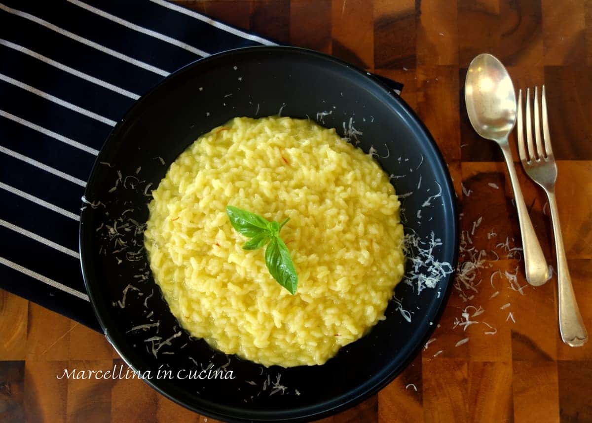 Saffron risotto with grated Parmesan cheese on a black plate with spoon and fork and black and white striped kitchen towel