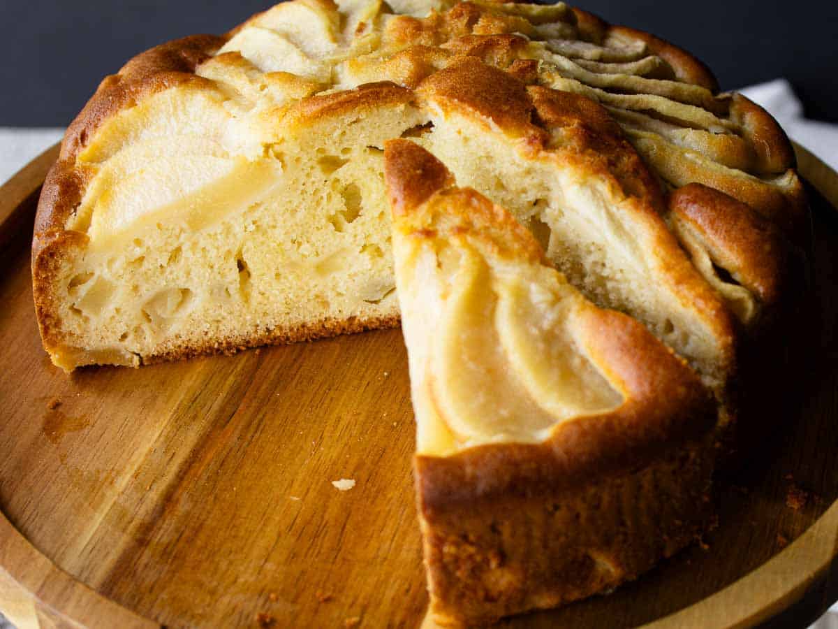 Cake with pear slices on top on a wooden cake stand with several wedges cut and removed.
