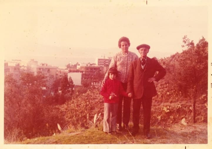 Vintage photo of old man, woman and small child with city in the background.