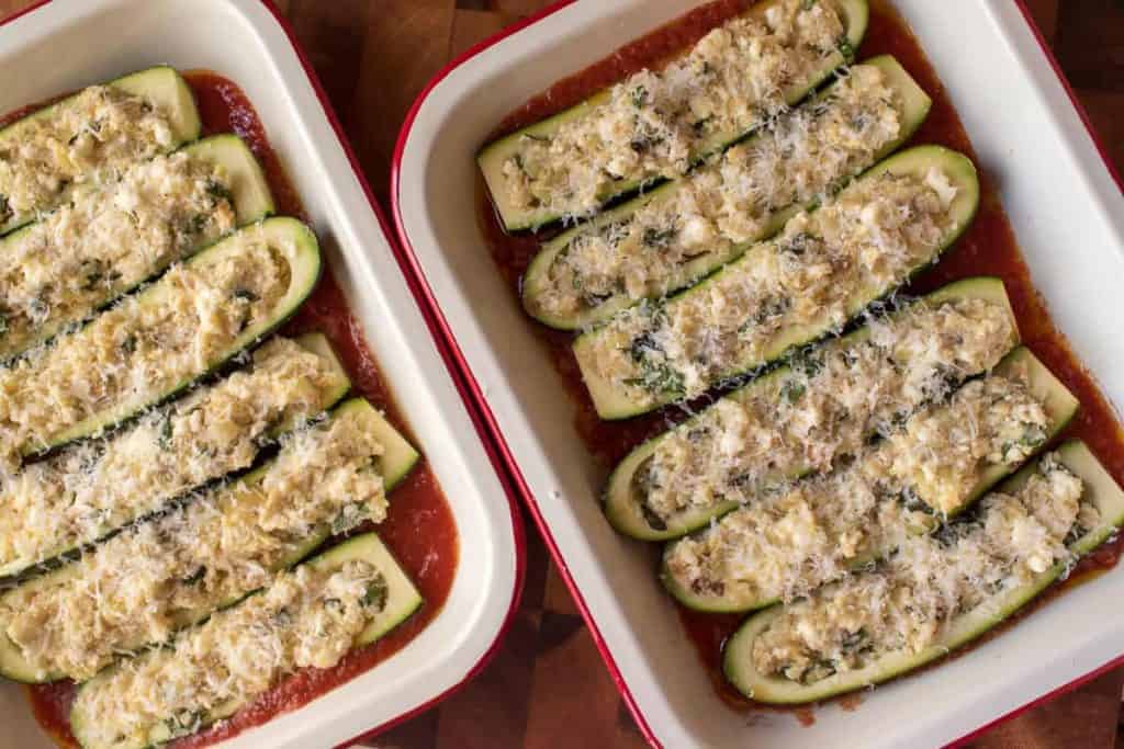 Two baking trays of unbaked zucchini with stuffed ricotta in tomato sauce.