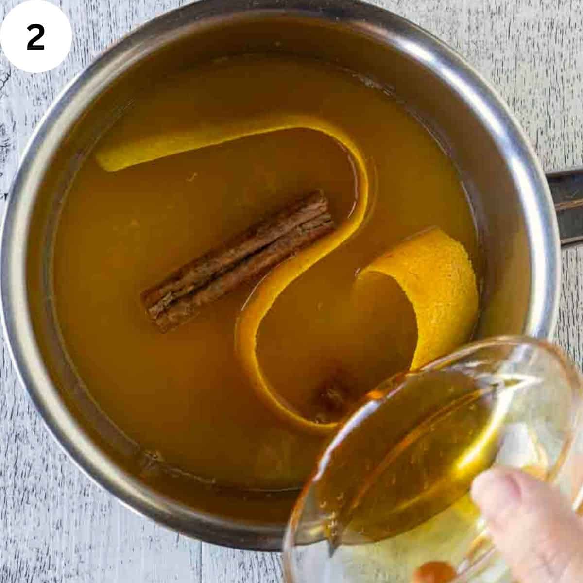Liquid in a saucepan with a strip of orange peel and a cinnamon sticks.