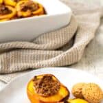 Baked Peaches on a white plate with more baked peaches in the background.