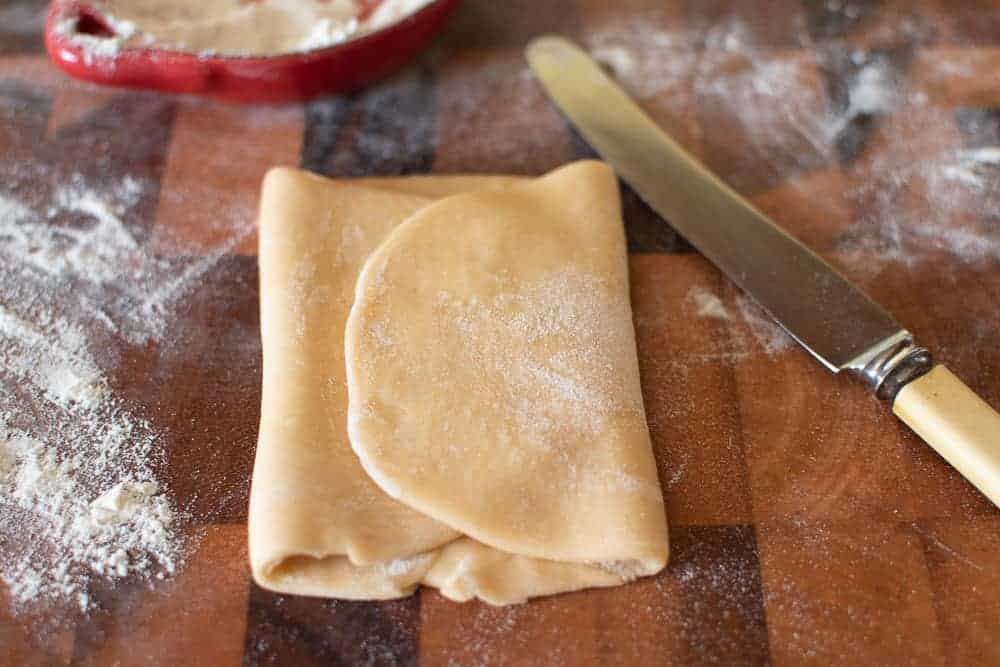 Making fresh pasta a home requires only two ingredients - flour and eggs. Learn how to make your own egg pasta with this step by step recipe. #homemade #homemadepasta #eggpasta #italianrecipe #pastarecipe Pasta dough folded, knife and flour.