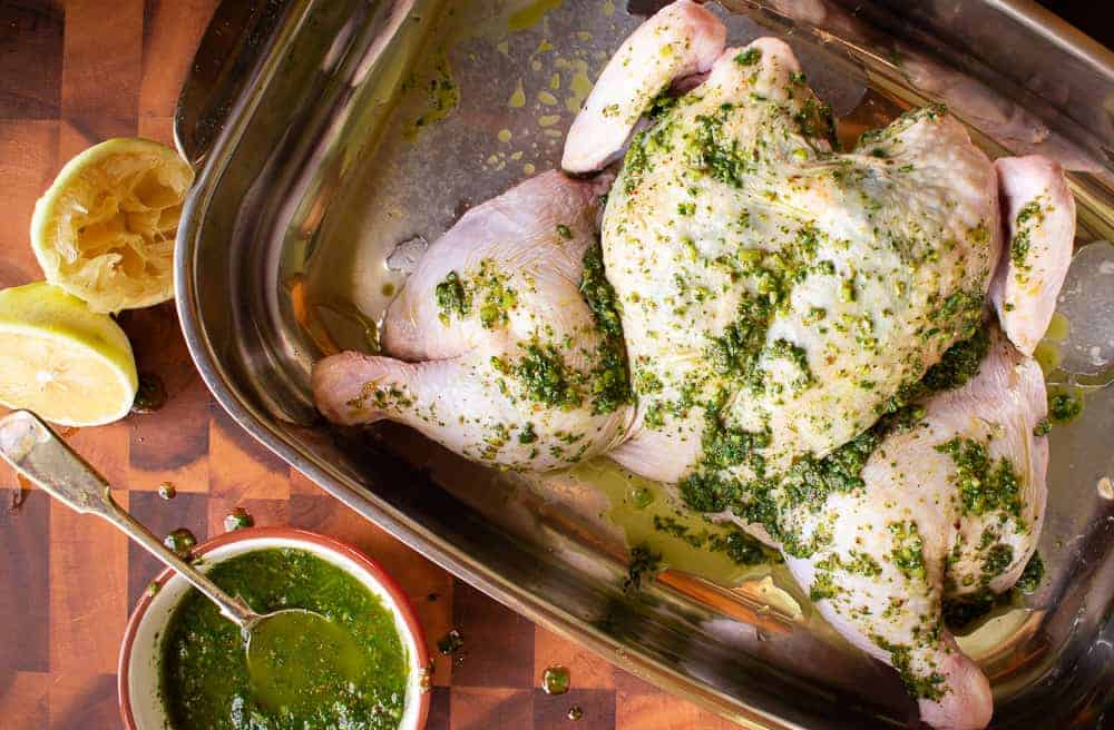 Raw whole butterflied chicken in baking dish spread with herb marinade.