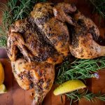 Roasted whole butterflied chicken on wooden board.