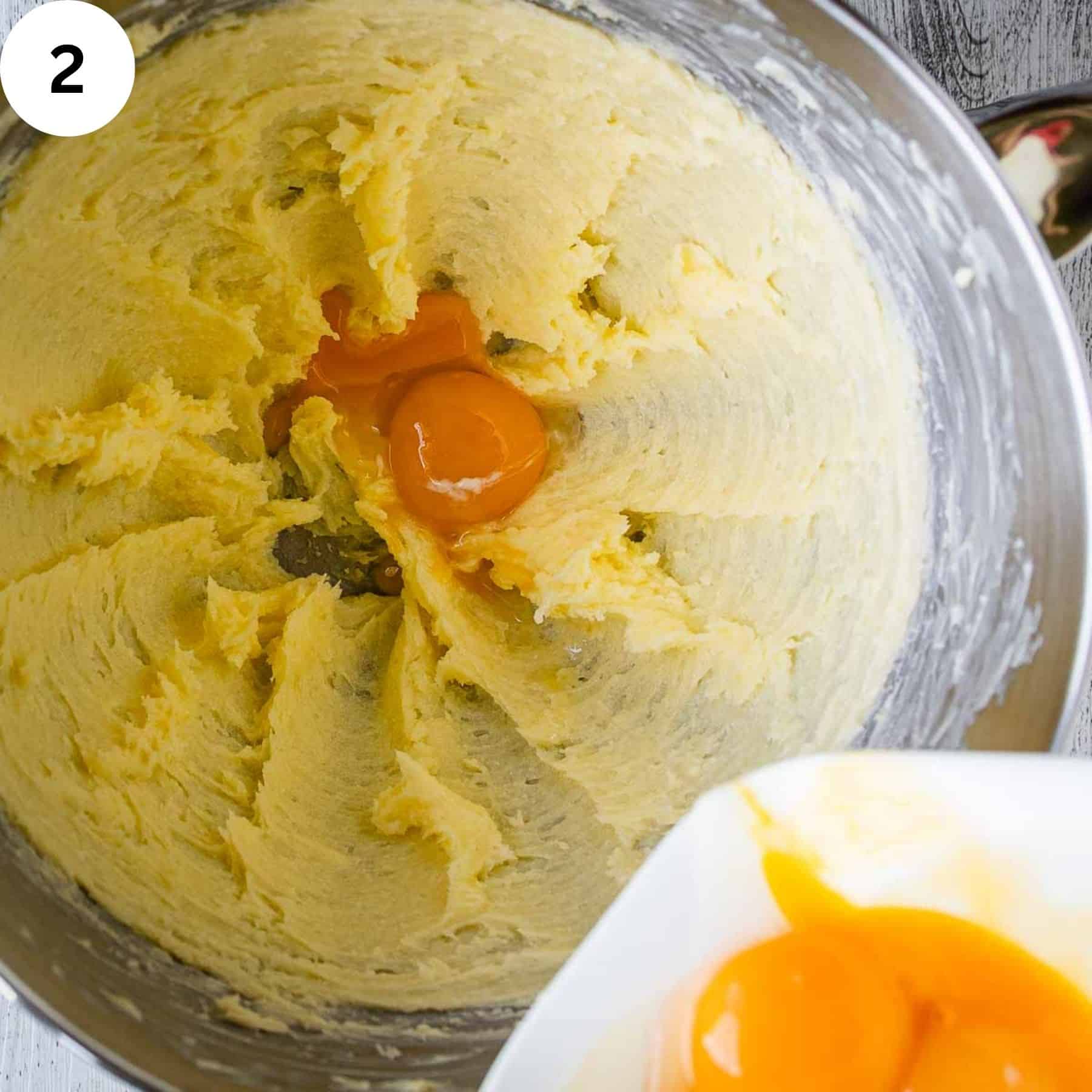 Egg yolks being added to creamy butter mixture in a bowl.