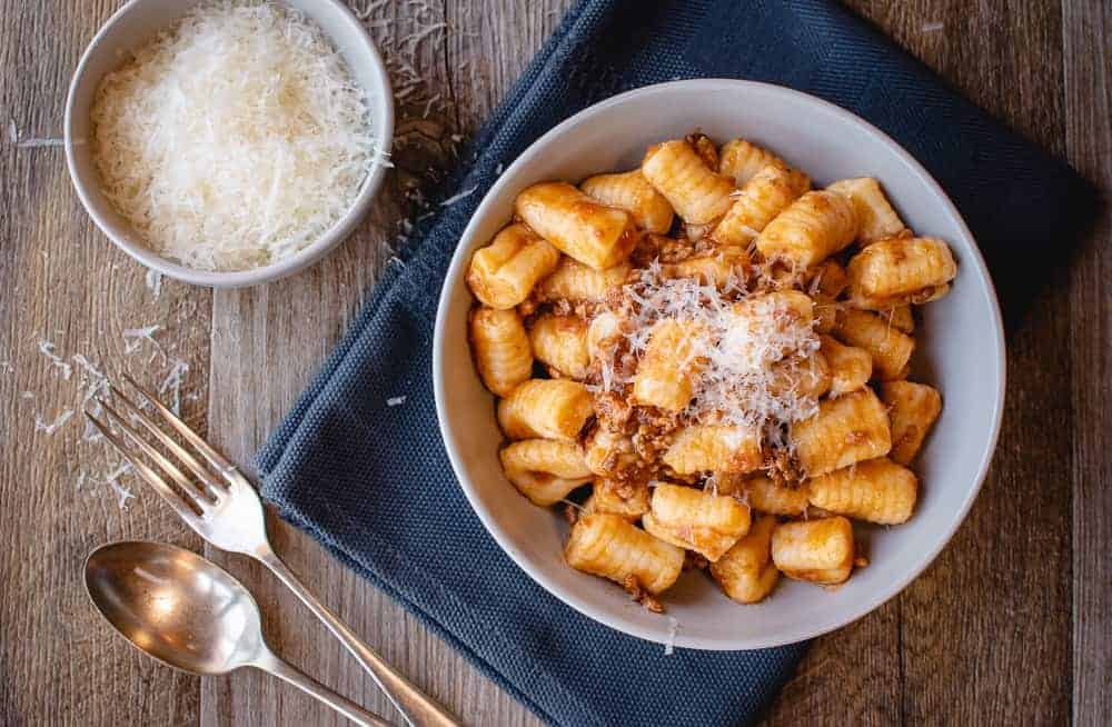 This Ragù Pasta Sauce has my father's secret ingredient that makes all the difference. This recipe makes a big batch so that you have lots to freeze for later. #ragu #pastasauce #italian #recipe white bowl of gnocchi on blue cloth