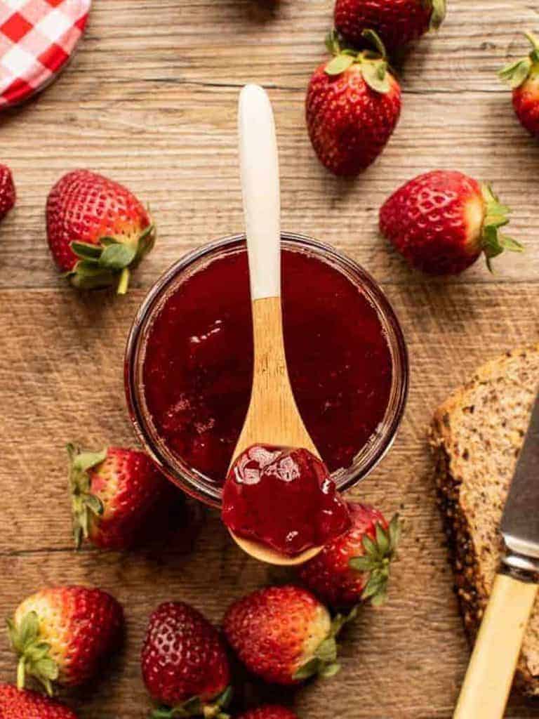 Jar of jam with strawberry jam on a spoon. strawberries and bread.