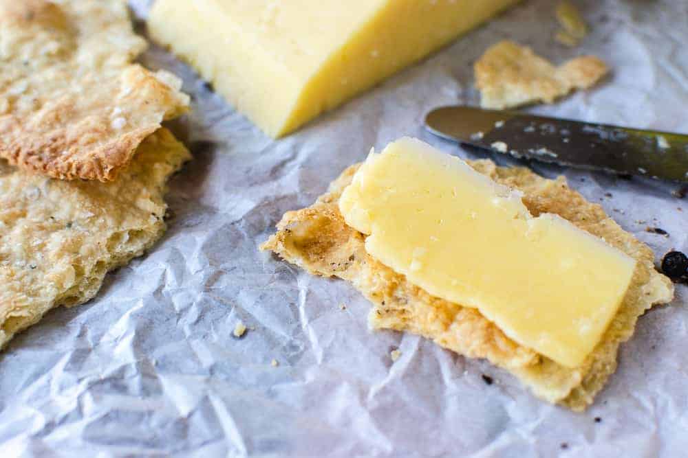 Homemade crackers are simply delicious, easy and so inexpensive to make. #homemadecrackers #crackers #cheese #artisan A cracker with cheese on top on baking paper.