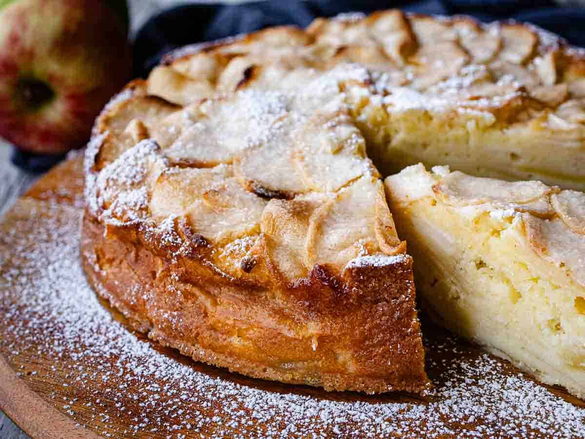 Moist Apple cake flavored with vanilla and lemon #applecake #cake #recipes #italianfood Cake with apples on a wooden board with a slice cut and revealed.