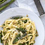 pasta with asparagus on white plate, fresh asparagus, block of cheese and grater