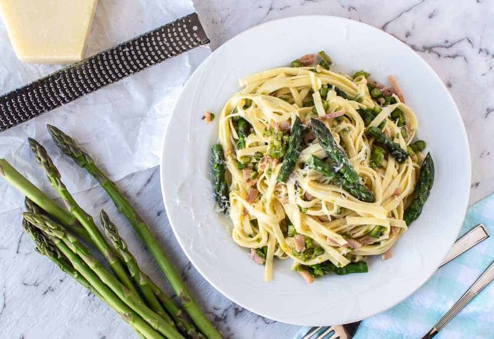 Pasta with Asparagus and bacon is perfectly simply pasta that is full of flavour. #pasta #asparagus #recipes #italianfood pasta with asparagus on white plate, fresh asparagus, block of cheese and grater