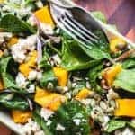 image with text. text read "roast pumpkin salad with spinach and feta". image is roast pumpkin salad with spinach leaves and feta viewed from above.