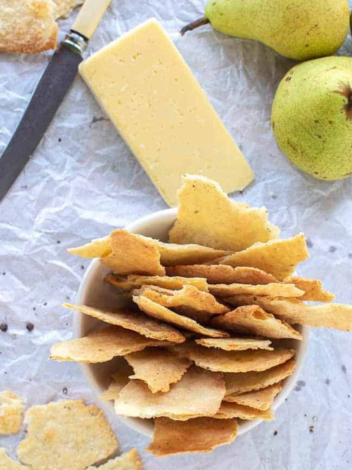 Homemade crackers in white bowl with cheese and green pears.