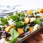 pumpkin and spinach salad on oblong plate on wooden board with plates and forks