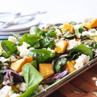pumpkin and spinach salad on oblong plate on wooden board with plates and forks