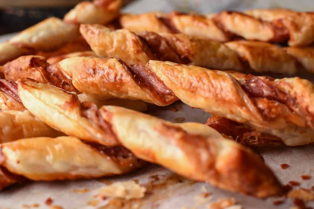 Crunchy Puff Pastry Twists with Prosciutto and Parmesan are delicious with drinks or as a snack. Plus so easy to make! #recipe #puffpastry #prosciutto #appetizer #snack #cheese close up of golden brown pastry twisted pastry.