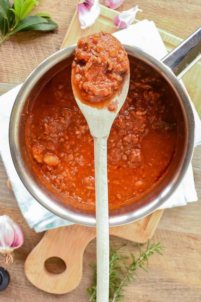Saucepan of ragu pasta sauce with wooden spoon resting across the saucepan with some ragu pasta sauce on the spoon