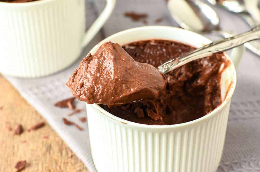 Chocolate pudding in a teacups with a heaped spoonful of pudding resting on the top of the cup.