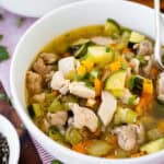 A bowl of chicken vegetable soup with bread.
