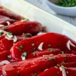 Italian Roasted Peppers on an oblong dish with slivers of fresh garlic and chopped parsley scattered on top.