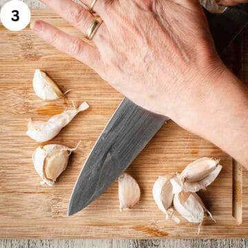 Unpeeled fresh garlic being crushed with the blade of a knife.