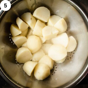 Parboiled peeled potatoes in a colander.
