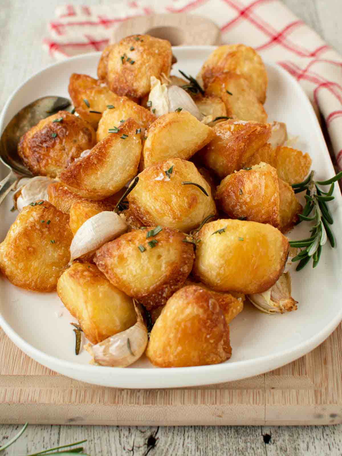 These crispy roast Potatoes are crispy and crunchy. Roasted with garlic and rosemary these potatoes are the perfect side dish. #roastedpotatoes #roasted #potatoes #sides Roasted Garlic and Rosemary Potatoes on a white oblong platter.