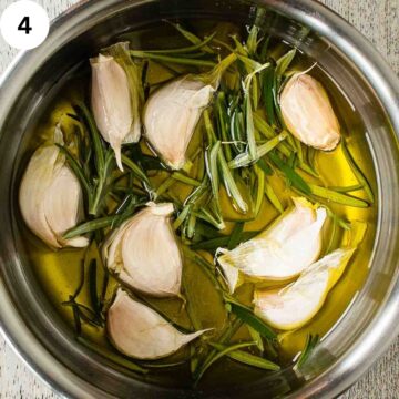 Whole garlic and fresh rosemary in a saucepan of oil.